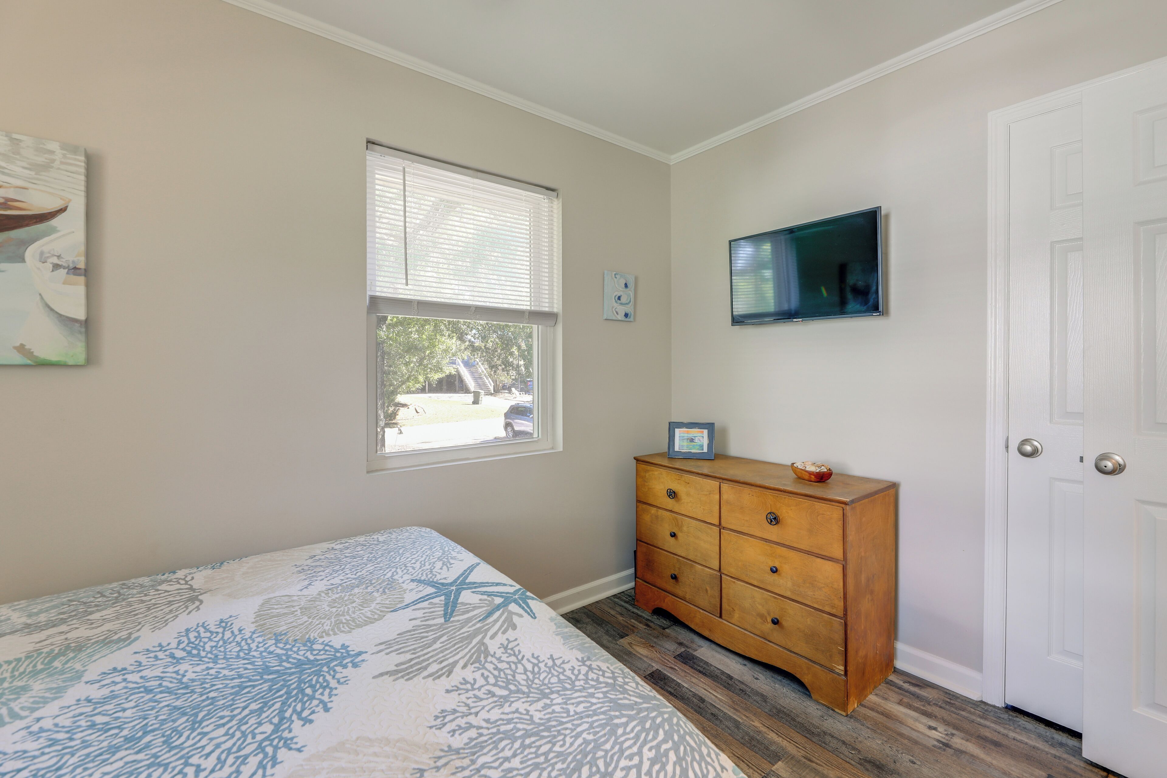 A bedroom with a bed, a wooden dresser, a television, and a window.