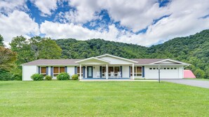 A two-story house with a front porch, a covered patio, and a red roof. - Near Hiking: Home w/ Trout Stream in Bakersville! (Bakersville)