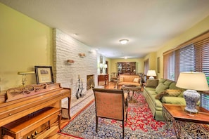 A living room with a fireplace, a piano, a sofa, and a patterned rug. - Near Hiking: Home w/ Trout Stream in Bakersville! (Bakersville)