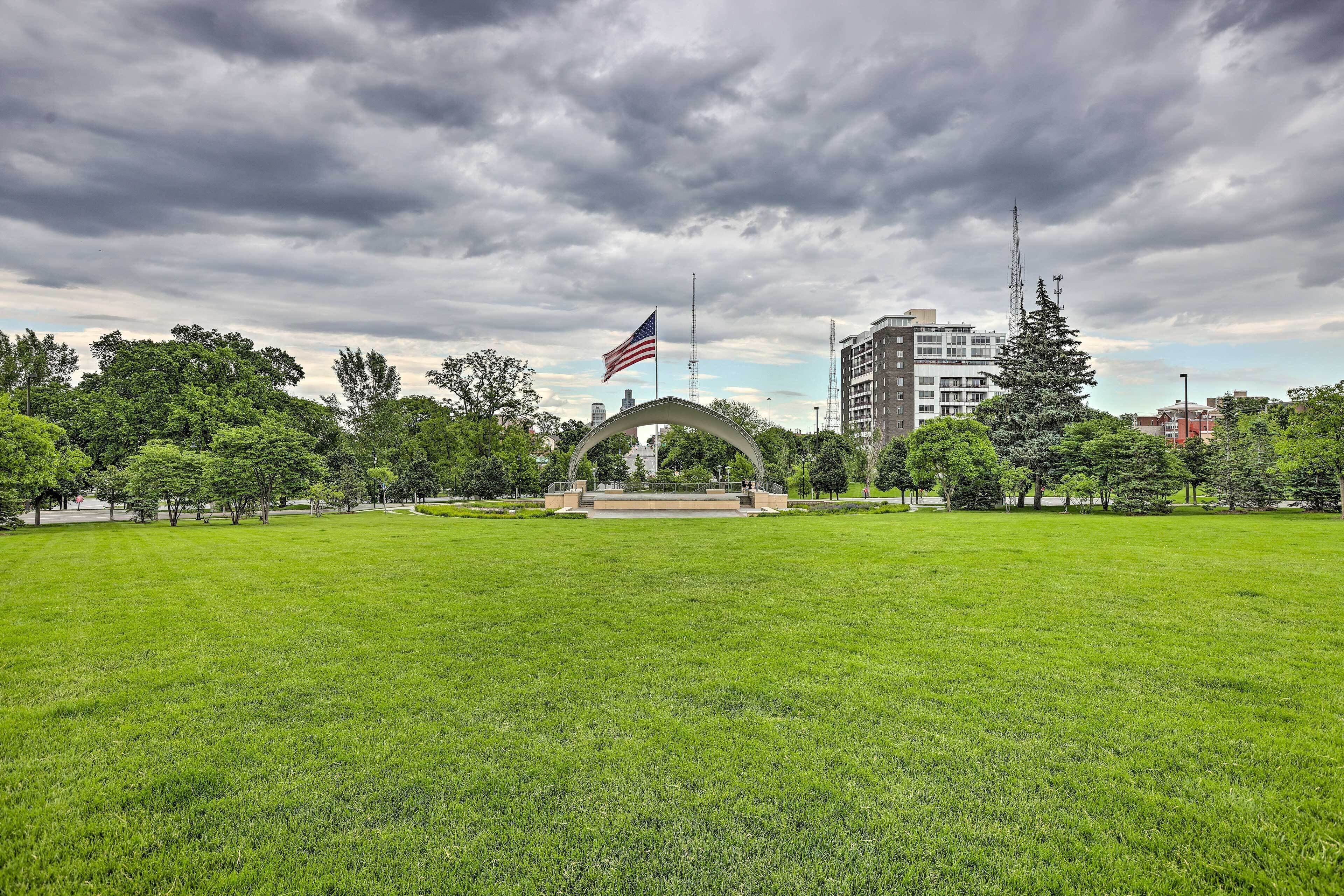 A park with a large grassy field, an American flag, and a building in the background.