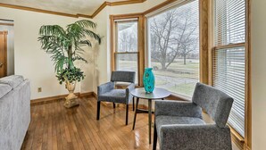 A corner room with wooden floors, two grey upholstered chairs, a round table, a turquoise vase, and a large potted plant. - 5-acre Vacation Home w/ Woods & Hiking Ground (Pickerington)