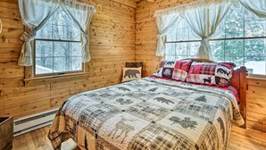 A wooden cabin bedroom with a bed, two windows with curtains, and a bear-themed pillow. - Andover Cabin Retreat w/ Hot Tub & Fireplace! (Chester)