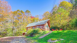 A log cabin with a porch, surrounded by autumn foliage and a dirt path leading to the entrance. - Andover Cabin Retreat w/ Hot Tub & Fireplace! (Chester)