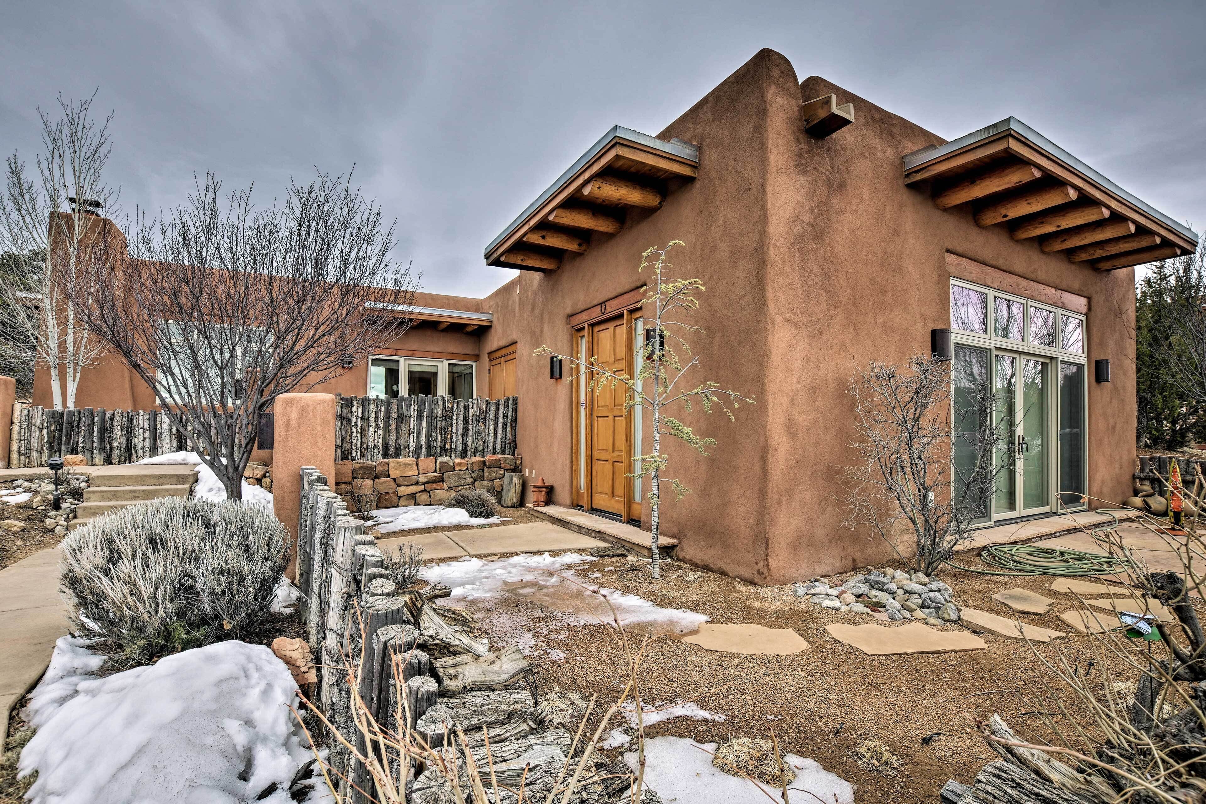 A stucco house with a wooden porch, a stone wall, and a small garden with snow patches.