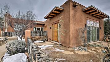 A stucco house with a wooden porch, a stone wall, and a small garden with snow patches.