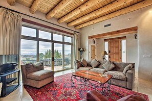 A spacious living room with a large window, a wooden ceiling, a sofa set, and a TV.