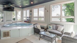 A spa area with a hot tub, wicker furniture, and large windows. - Hot Tub + Private Beach: Waterfront Urbanna Escape (Urbanna)