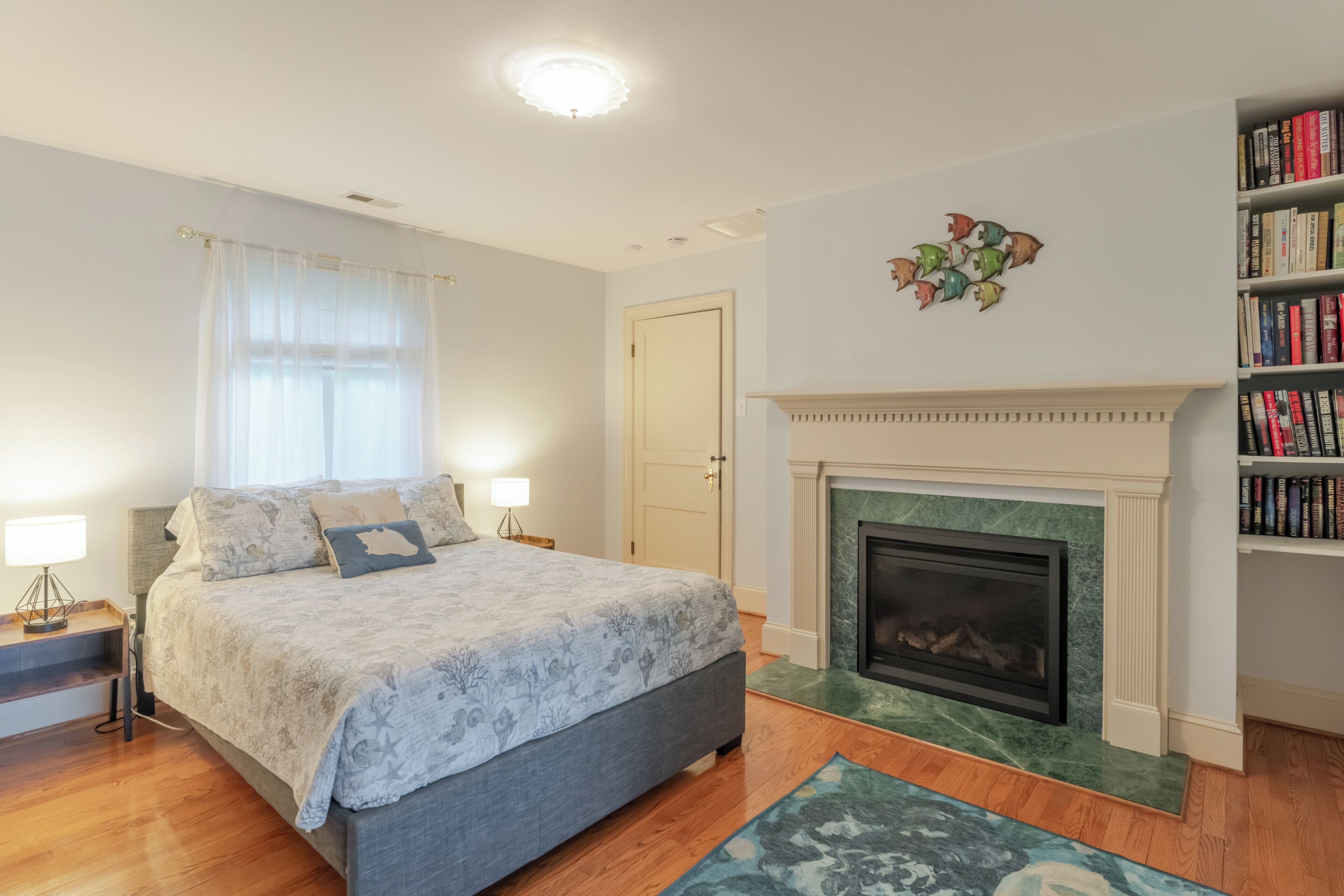 A bedroom with a large bed, a fireplace, a bookshelf, and a door.