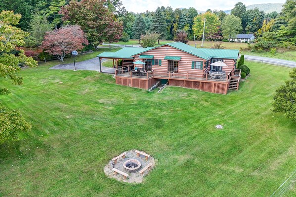 A large, two-story log cabin with a green roof, a deck, and a fire pit in the yard.