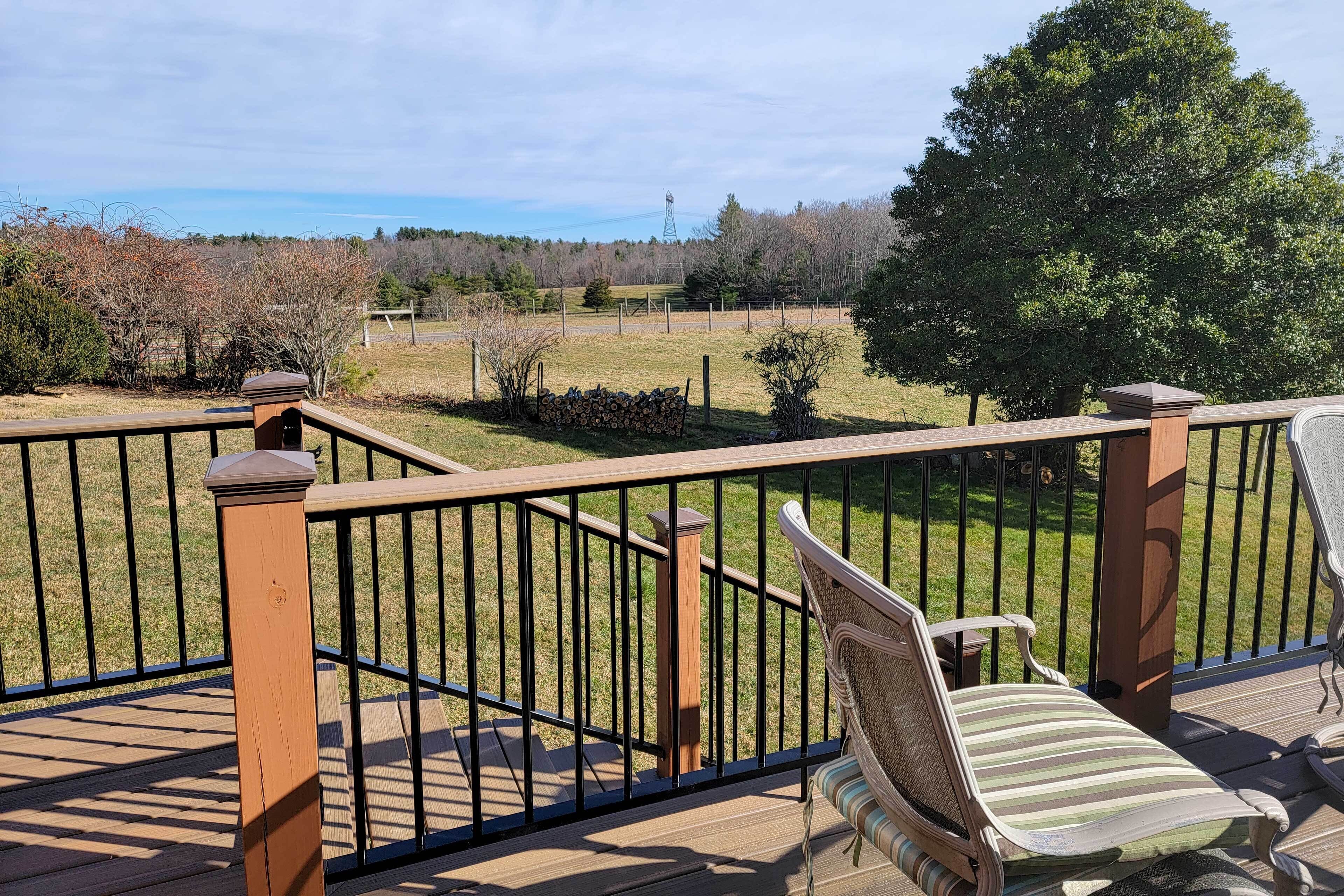 A deck with a wooden railing, a chair, and a view of a grassy field and trees.