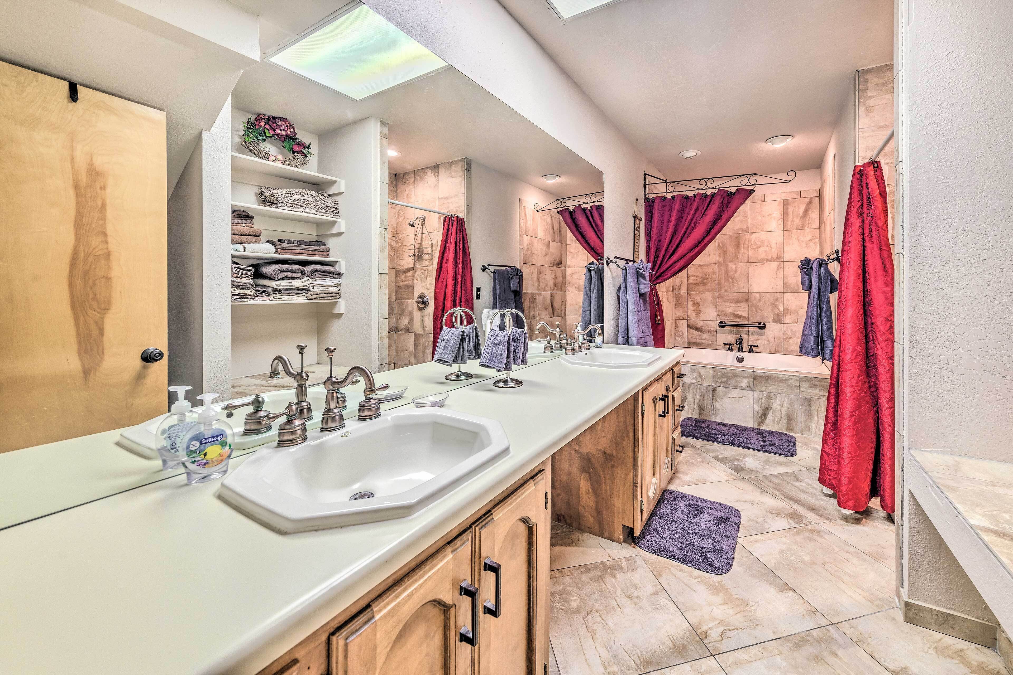 A modern bathroom with a large vanity, dual sinks, a shower area, and a built-in shelf with towels.