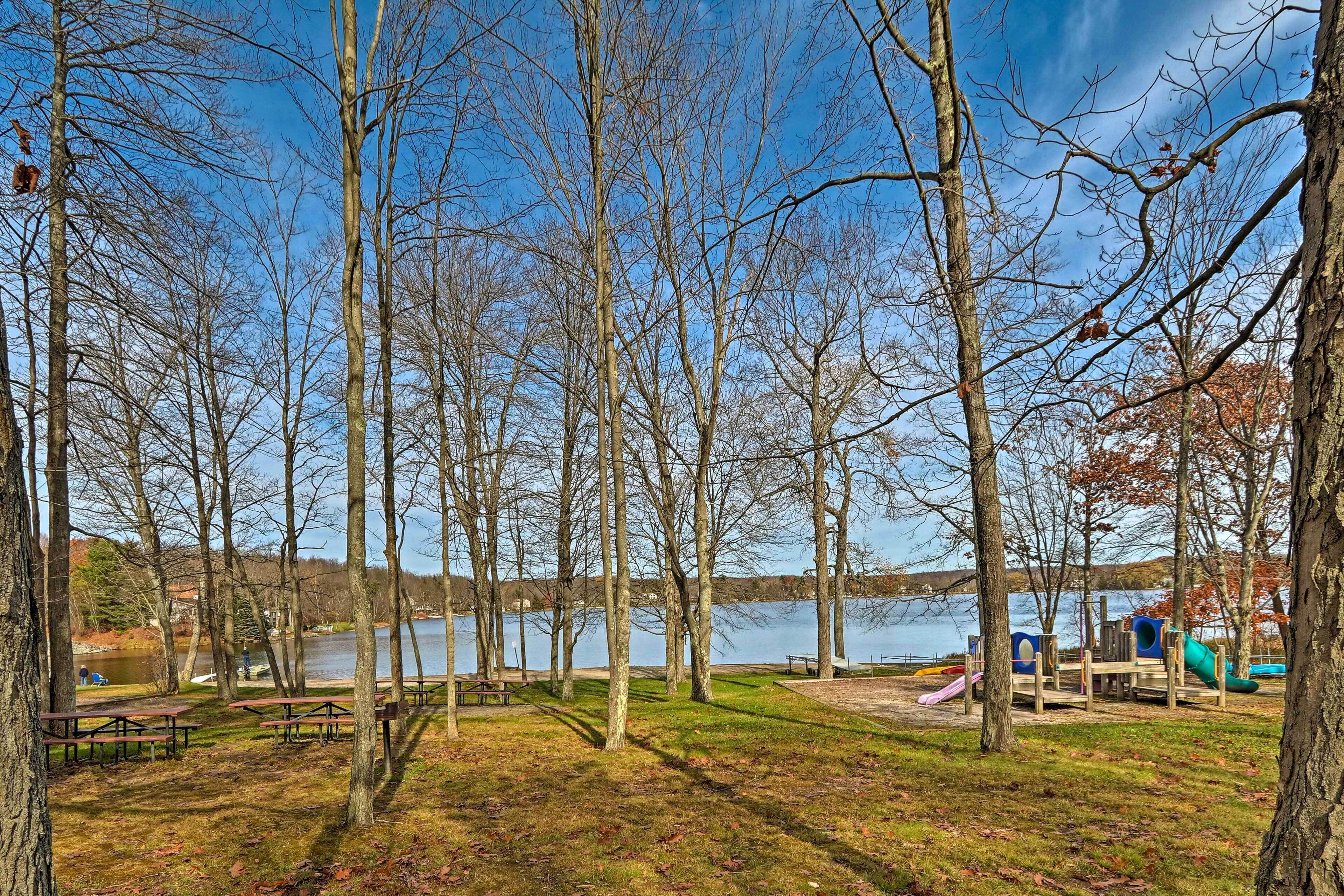 A park with picnic tables, a playground, and a lake in the background.