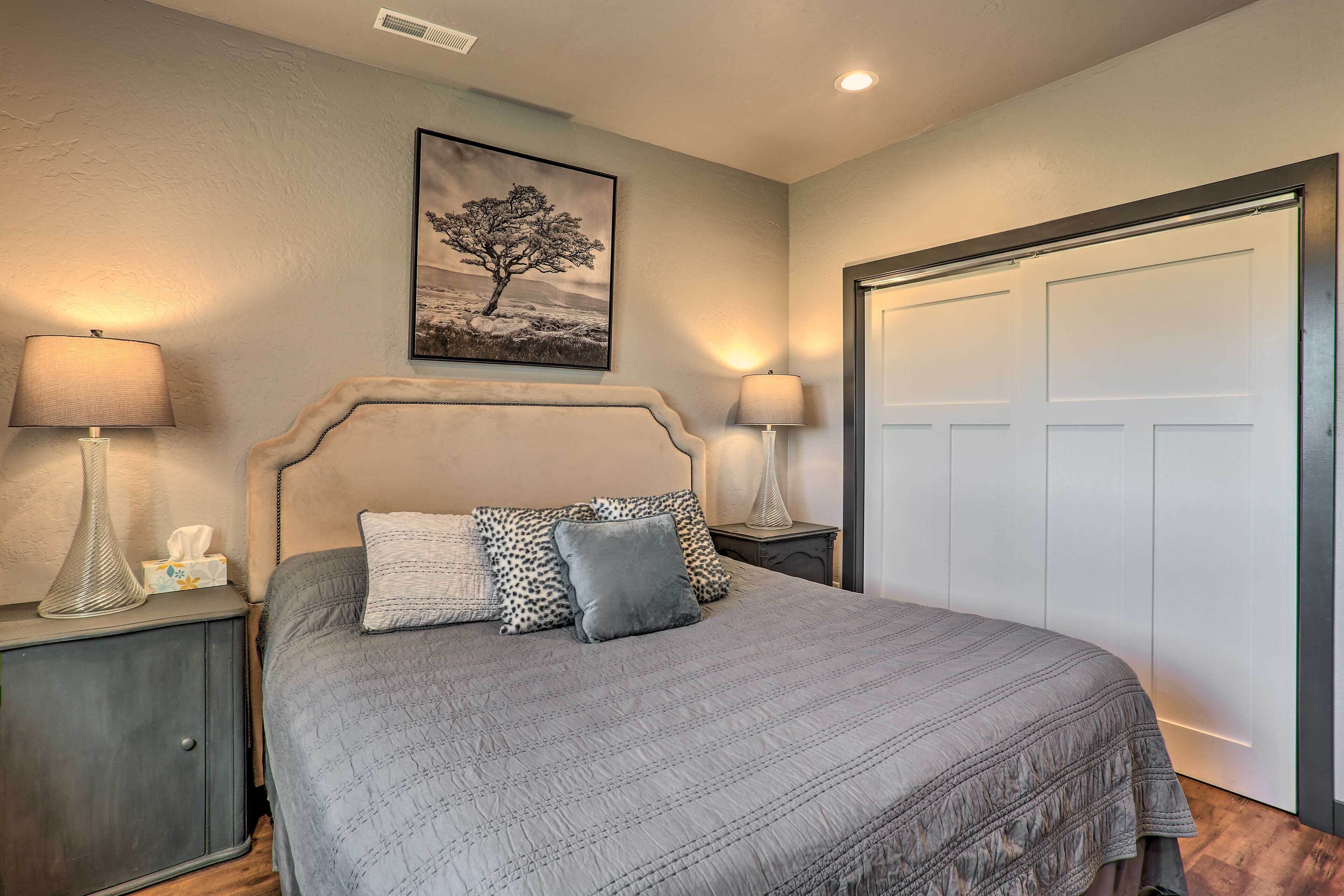 A bedroom with a bed, two bedside lamps, a nightstand, a framed picture on the wall, and a closet with a door.