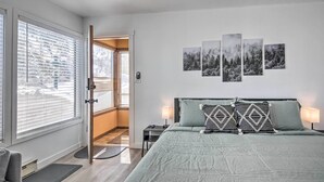 Quarto com cama, mesa de cabeceira, janela com persianas e arte nas paredes.