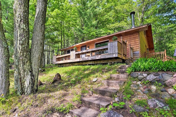A cabin with a wooden exterior, built on a stone foundation, surrounded by trees and a stone staircase. - Burns Lake Cabin w/ Dock, Fire Pit, Rowboat & More (Hayward)