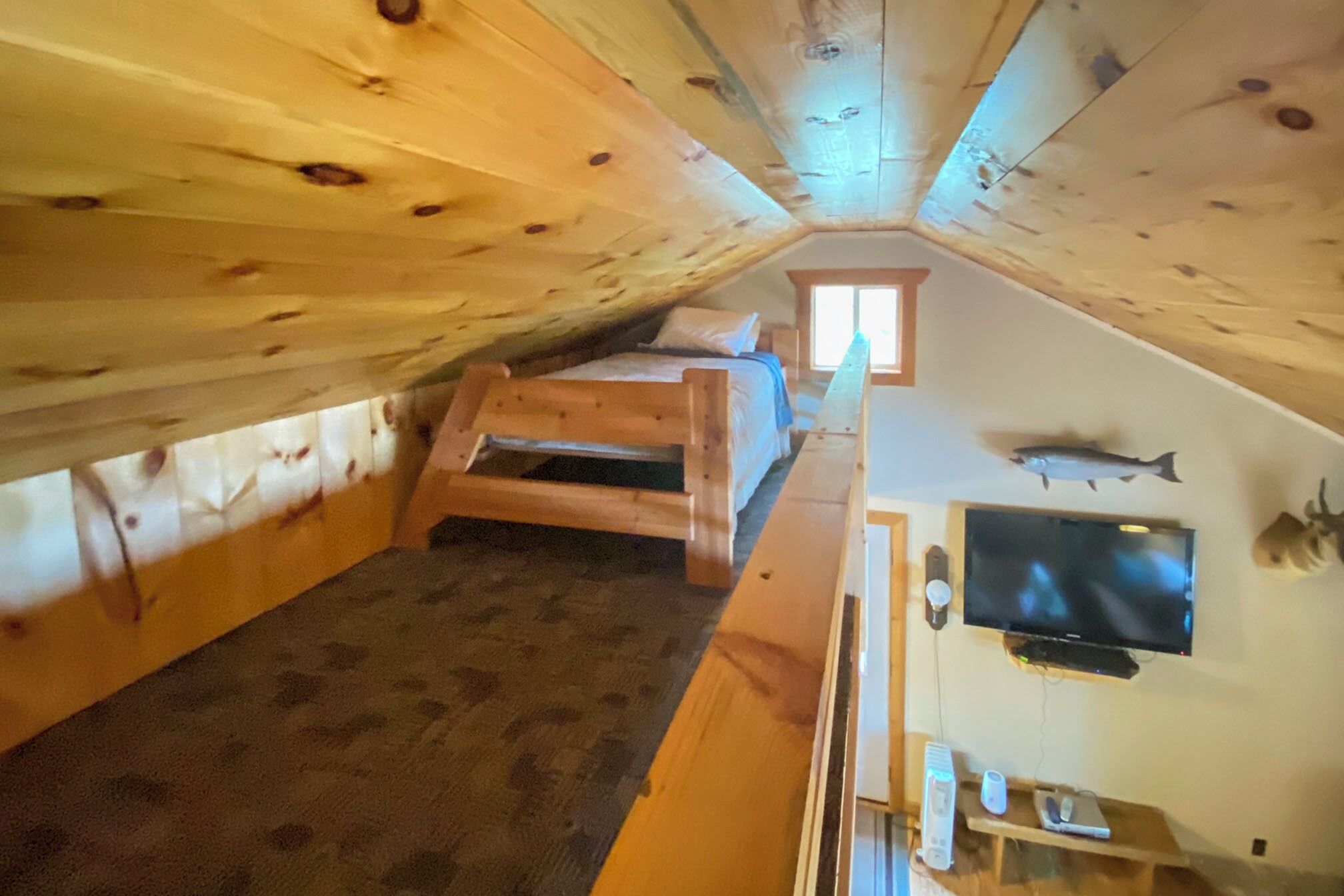 Un dormitorio acogedor en el ático, con una cama litera, un televisor y un pez montado en la pared.