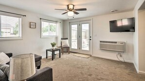 A living room with a ceiling fan, a flat-screen TV mounted on the wall, and a large window with blinds. - Cañon City Home: 15 Mi to Royal Gorge Bridge! (Canon City)