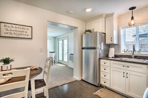 Una cocina con armarios blancos, un refrigerador de acero inoxidable, una zona de comedor con mesa y sillas, y una cita inspiradora enmarcada en la pared.