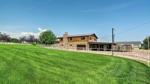 A two-story log cabin with a stone chimney, a covered porch, and a fenced yard. - Cañon City Home: 15 Mi to Royal Gorge Bridge! (Canon City)