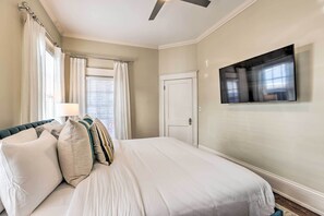 Een slaapkamer met een bed, gordijnen, een flatscreen televisie en een deur.