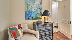 A room with a beige armchair, a black and gold side table, a colorful throw pillow, and a large abstract painting on the wall.