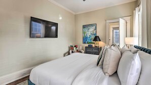 A hotel room with a large bed, a flat-screen TV mounted on the wall, a painting on the wall, a desk with a lamp, and a chair.