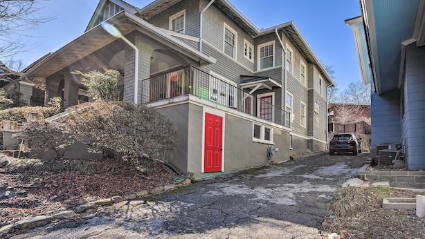 A two-story house with a red door, a balcony, and a driveway leading to a parked car.