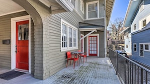 A residential building with a red door, a covered porch, and a small outdoor seating area with red chairs.