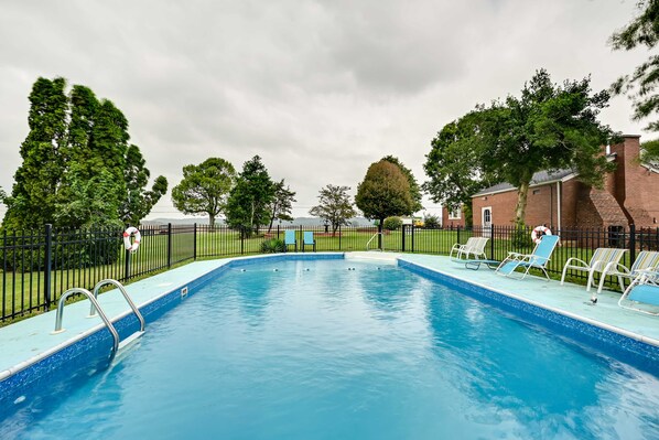 A rectangular swimming pool with a blue tiled edge, surrounded by a black metal fence.