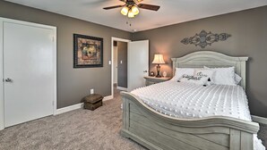 A bedroom with a bed, a ceiling fan, a nightstand with a lamp, a framed picture on the wall, and a door.