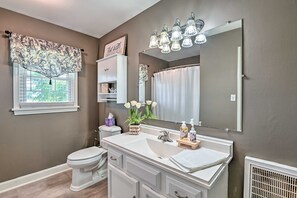 A bathroom with a vanity, toilet, and a window with a decorative valance.
