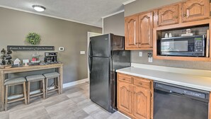 A compact kitchen with a refrigerator, microwave, and dishwasher. There is a wooden countertop and a small bar area with stools.