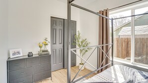 A bedroom with a metal bed frame, a grey dresser, a window with curtains, and a potted plant.