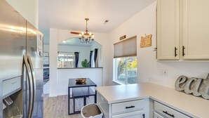 A modern kitchen with white cabinetry, a stainless steel refrigerator, a chandelier, and a window with a view of a fence.