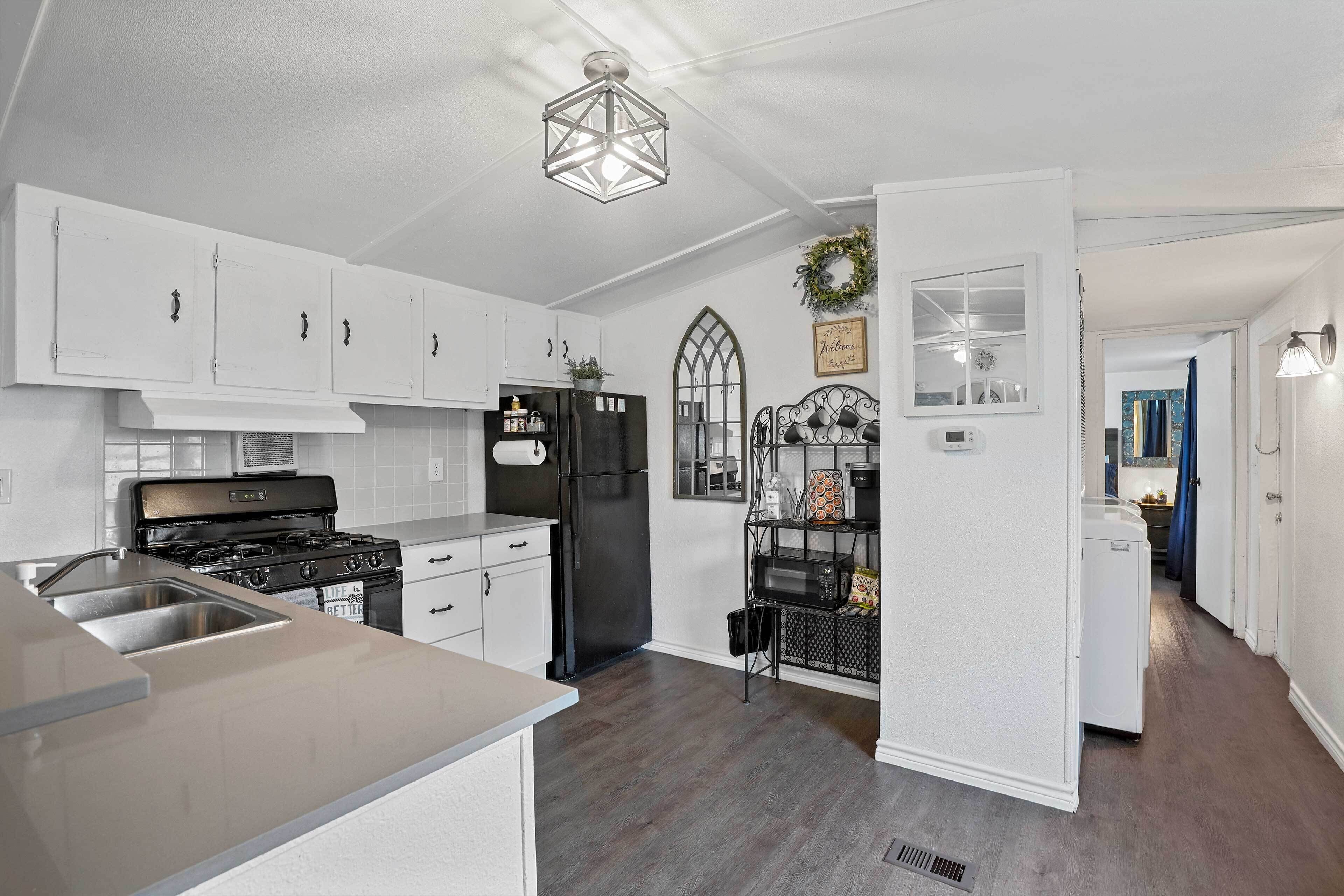 A modern kitchen with white cabinetry, a black stove, and a black refrigerator. There is a built-in oven, a sink, and a window with a decorative wreath.