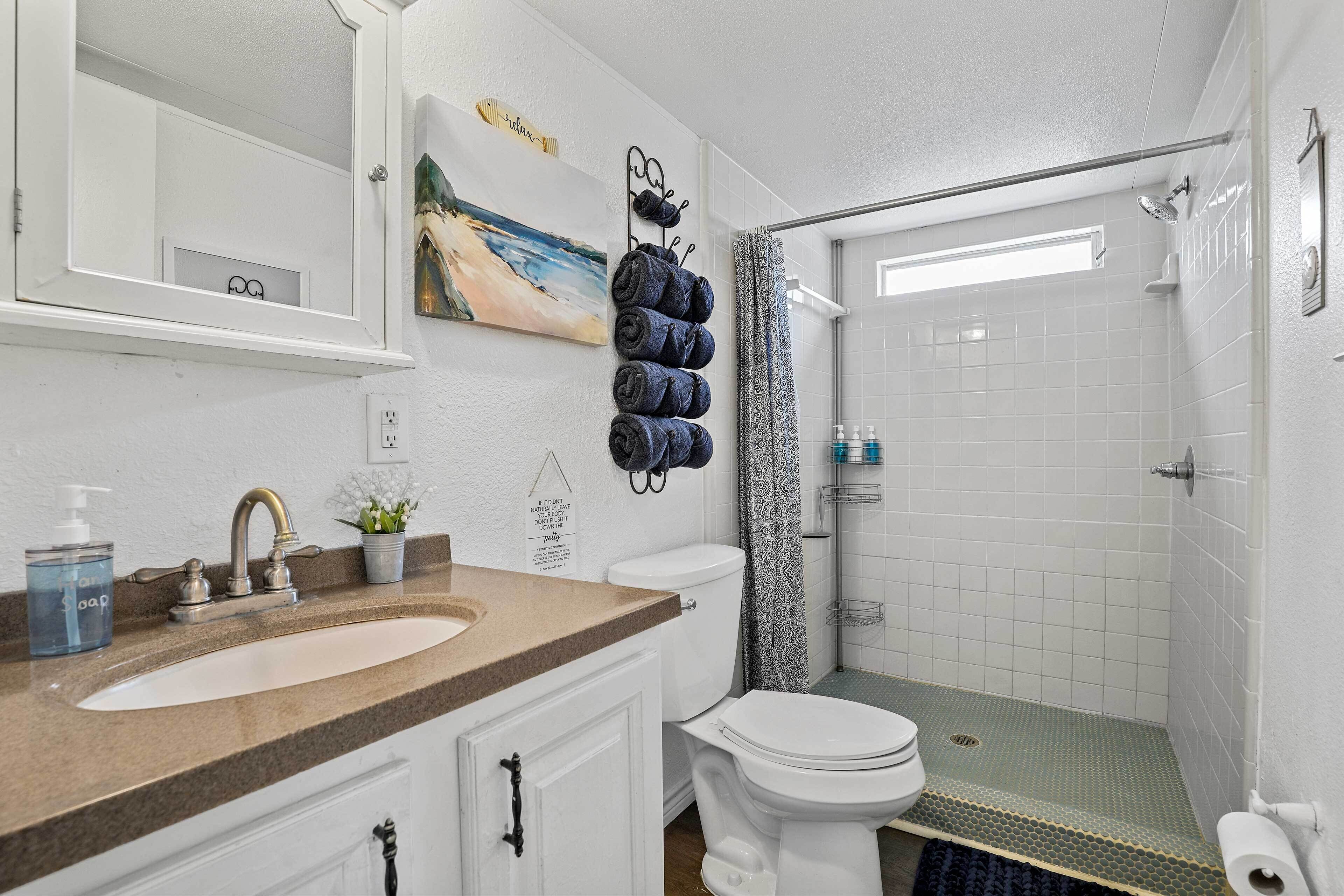 Un baño con lavamanos blanco, inodoro, ducha con puerta de vidrio y toallas colgadas en un perchero.