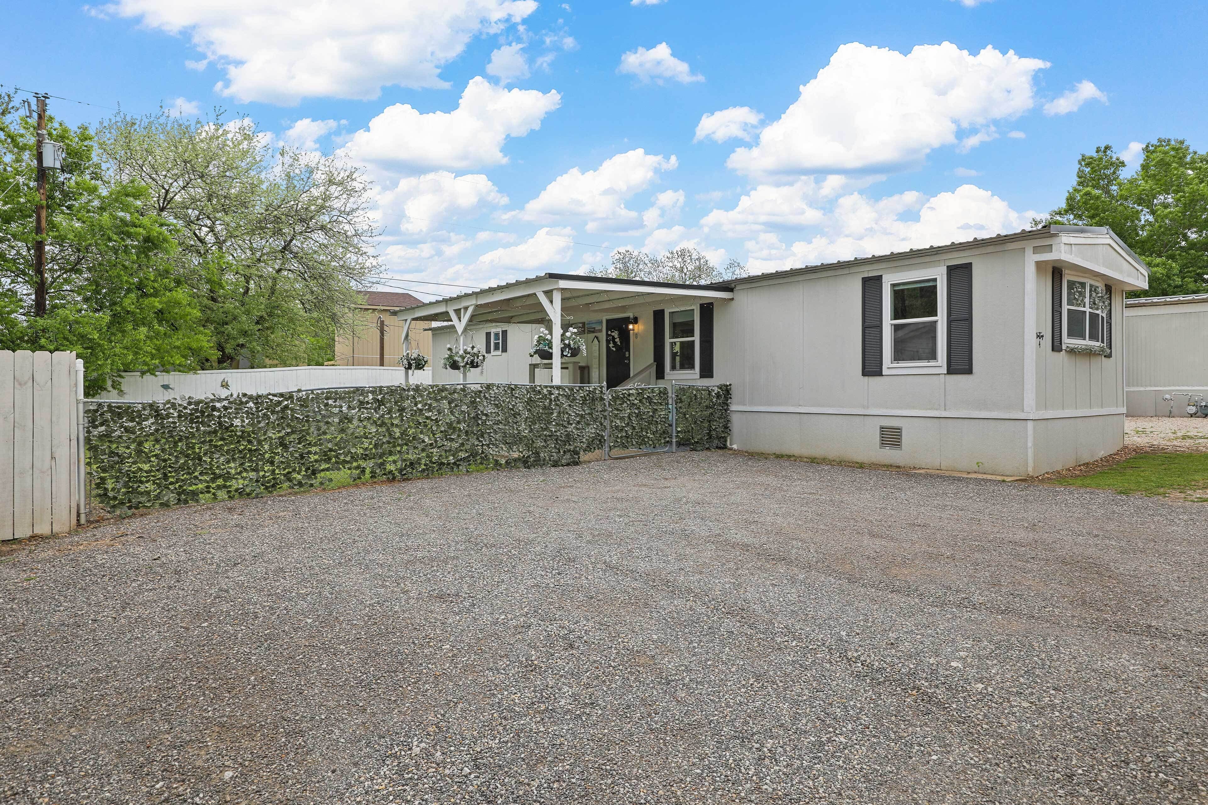 A single-story mobile home with a gravel driveway and a stone wall.