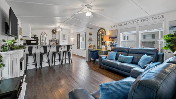 A spacious living area with a dark leather sofa, a dining table with bar stools, and a kitchen area. - Near Water: Lake Dallas Home w/ Furnished Patio! (Lake Dallas)
