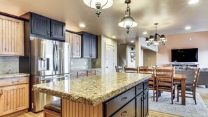 A kitchen with wooden cabinets, a stainless steel refrigerator, granite countertops, and a dining area with chairs and a table. - Private Beach Access! Luxe 7BR Bear Lake Cabin (Garden City)