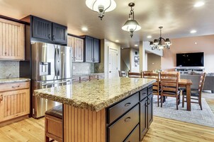 Una cocina con armarios de madera, refrigerador de acero inoxidable, encimeras de granito y una zona de comedor con sillas y una mesa.