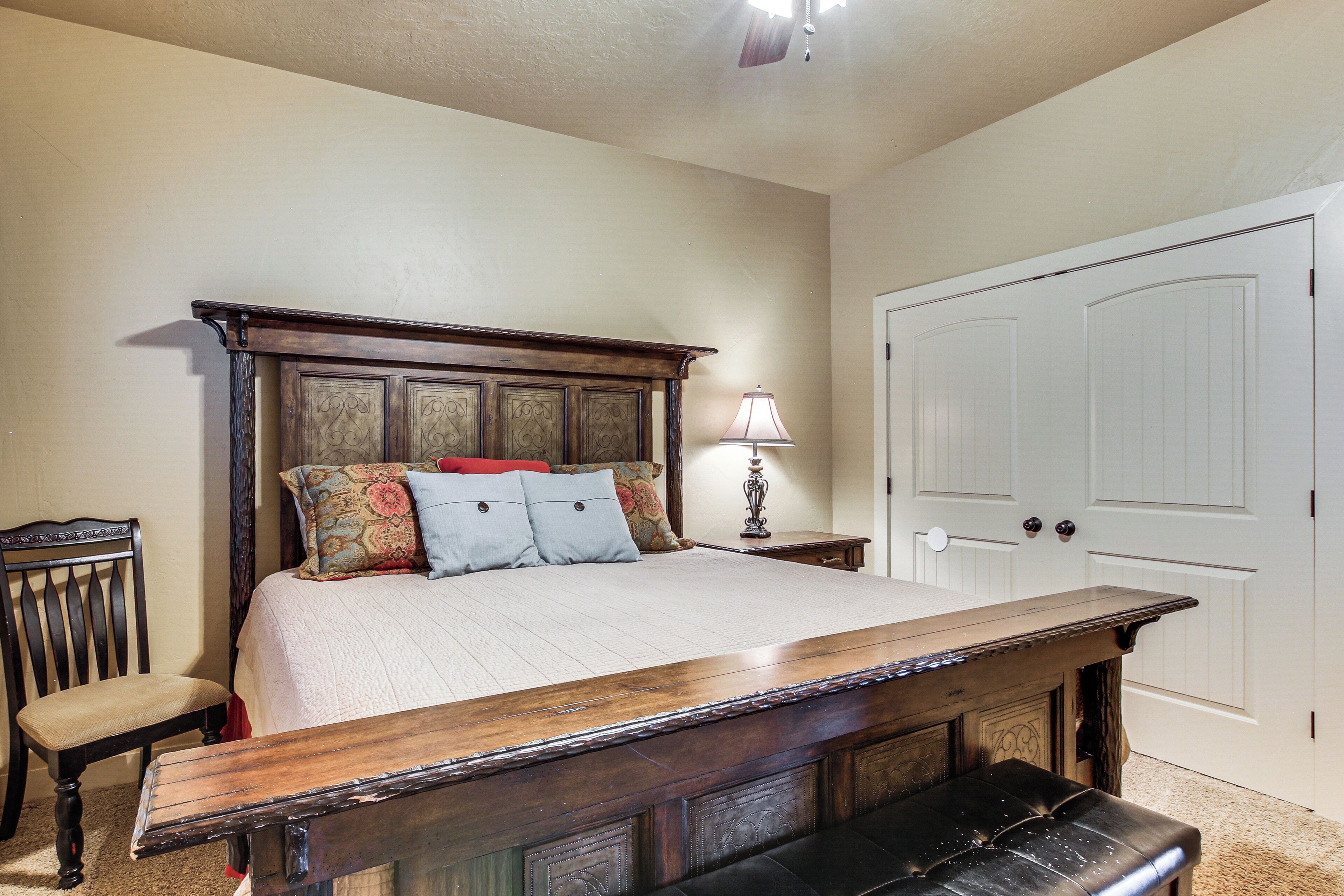 Une chambre à coucher avec un grand lit, un banc en bois, une chaise, une table de chevet avec une lampe et une porte blanche.