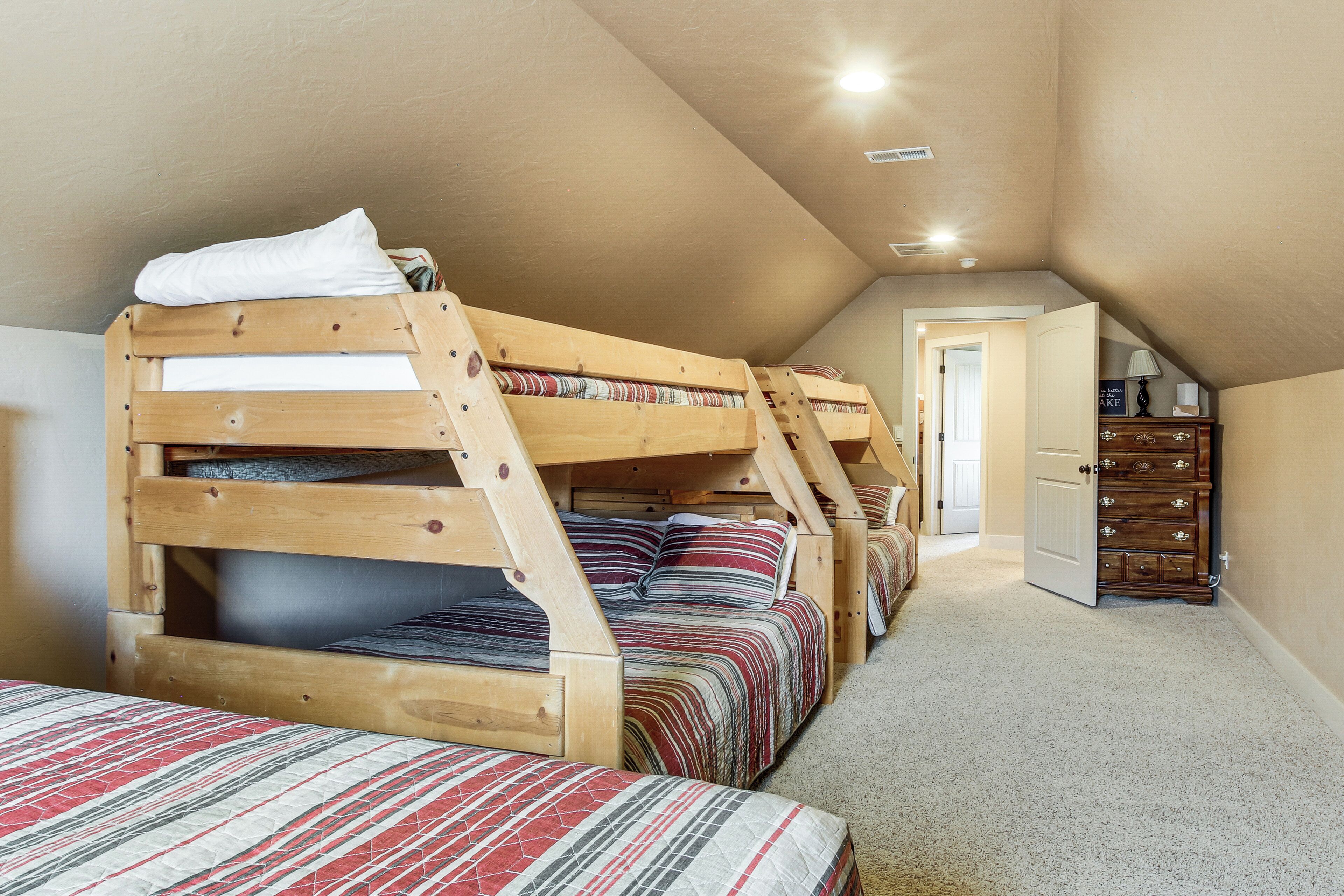 A dormitory room with bunk beds, a dresser, and a door leading to another room.