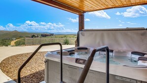 A hot tub with a wooden pergola overhead, surrounded by a landscaped area with a view of distant houses and hills. - Private Beach Access! Luxe 7BR Bear Lake Cabin (Garden City)