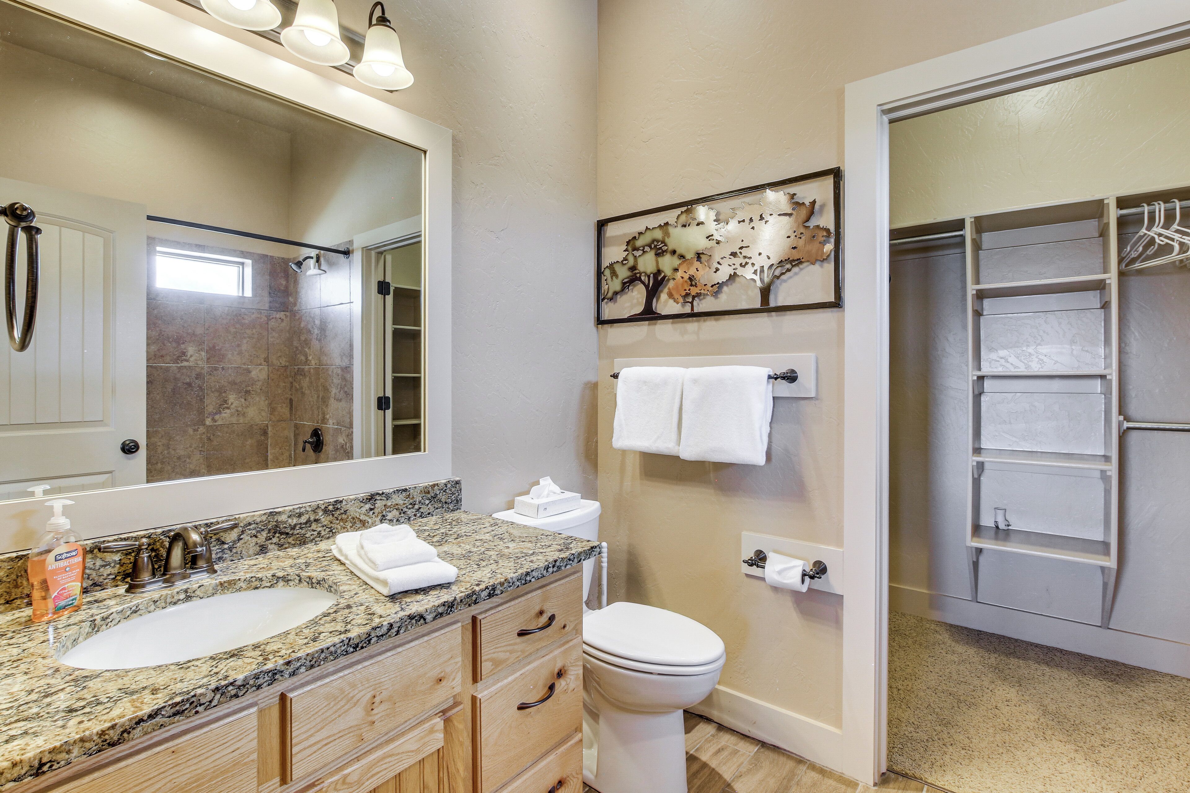 A bathroom with a granite countertop sink, a large mirror, a toilet, and a towel rack.