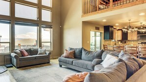 A spacious living area with a large sectional sofa, a dining table, and a kitchen in the background. - Private Beach Access! Luxe 7BR Bear Lake Cabin (Garden City)