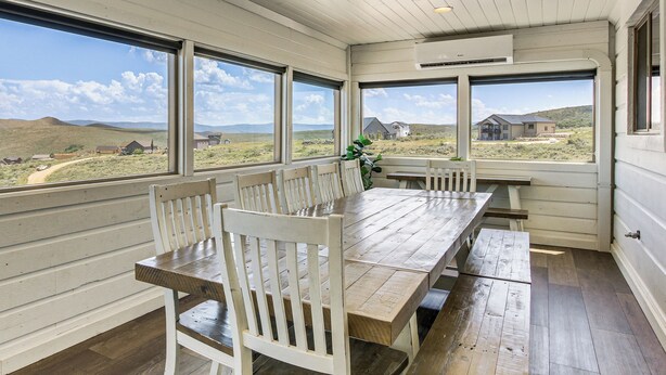 A dining area with a wooden table and chairs, large windows with a view of the countryside, and a white ceiling. - Private Beach Access! Luxe 7BR Bear Lake Cabin (Garden City)