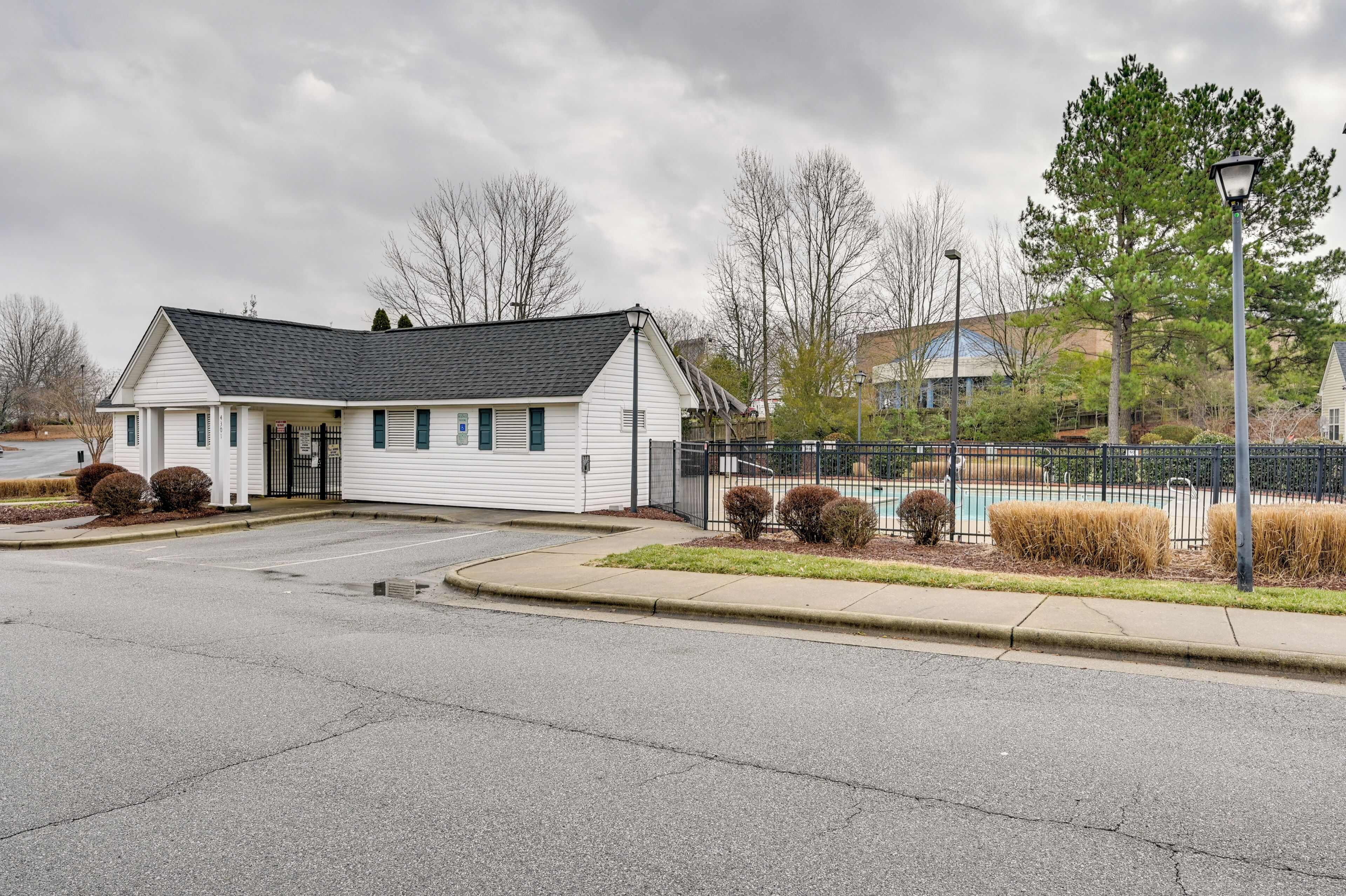 A single-story white building with a dark roof, a gated entrance, and a paved driveway.