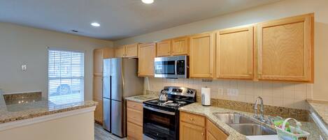 A kitchen with wooden cabinets, stainless steel appliances, granite countertops, and a window with blinds.