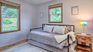 Ein Schlafzimmer mit Bett, zwei Fenstern, einem Nachttisch und einem Deckenventilator.