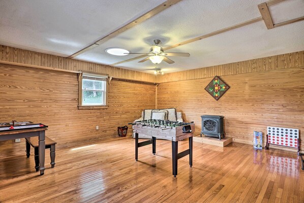 A room with wooden walls, a ceiling fan, a foosball table, a vintage stove, and a pinball machine.